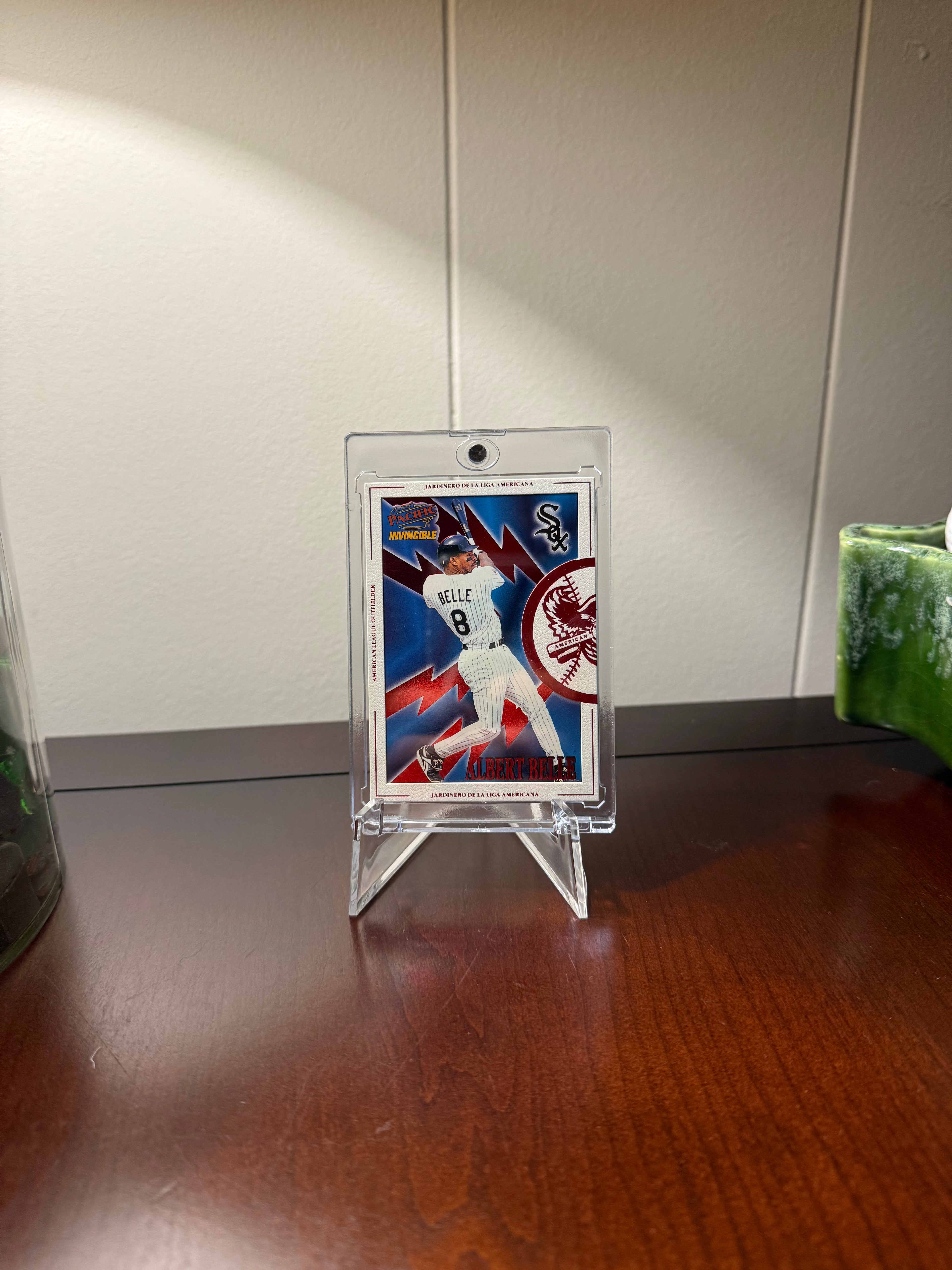 Baseball trading card of Albert Belle in a clear one touch holder suspended with a cheap acrylic plastic stand on a wooden surface with a neutral background