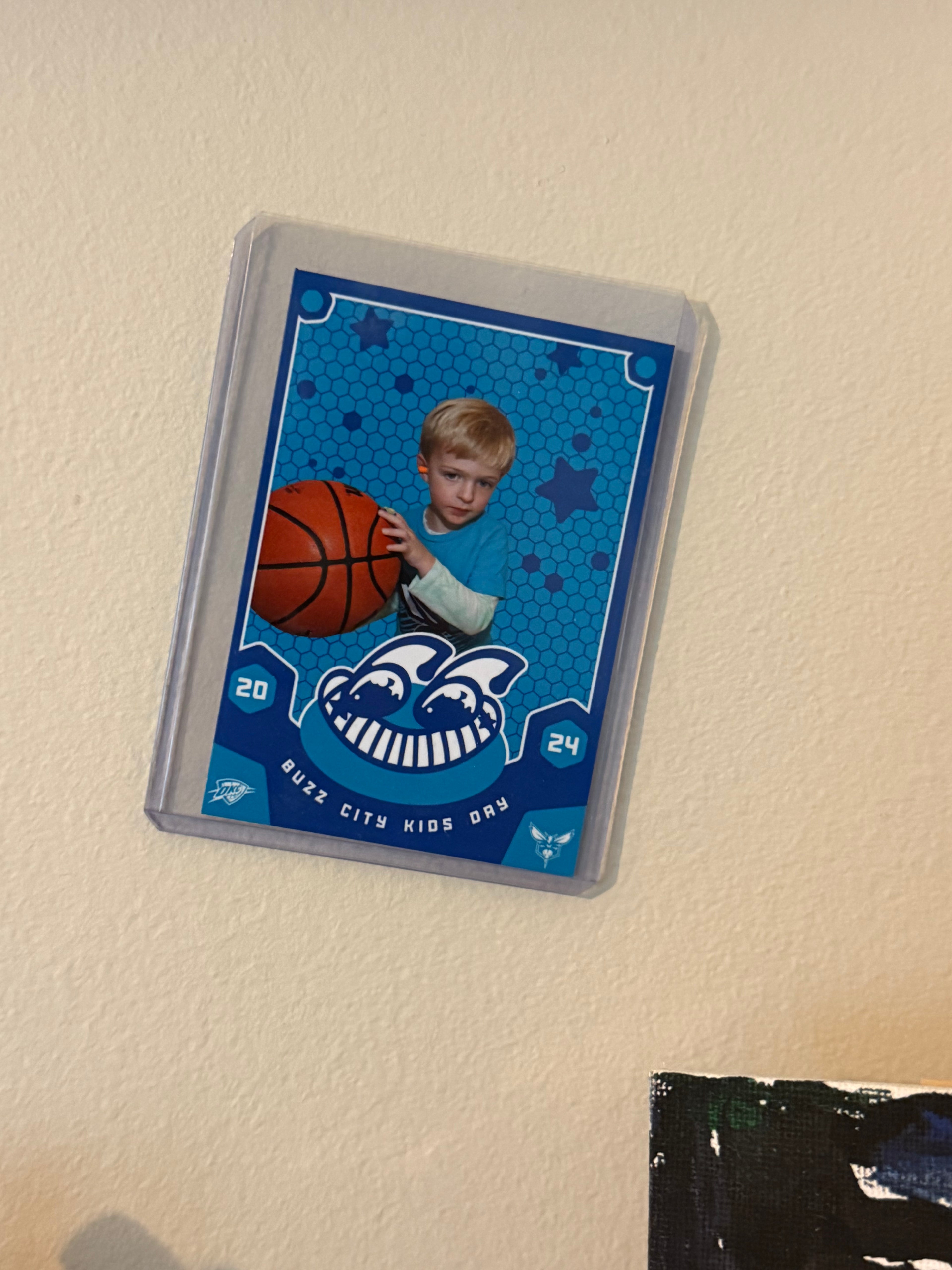 Trading card of a child holding a basketball with a blue border on a beige wall.