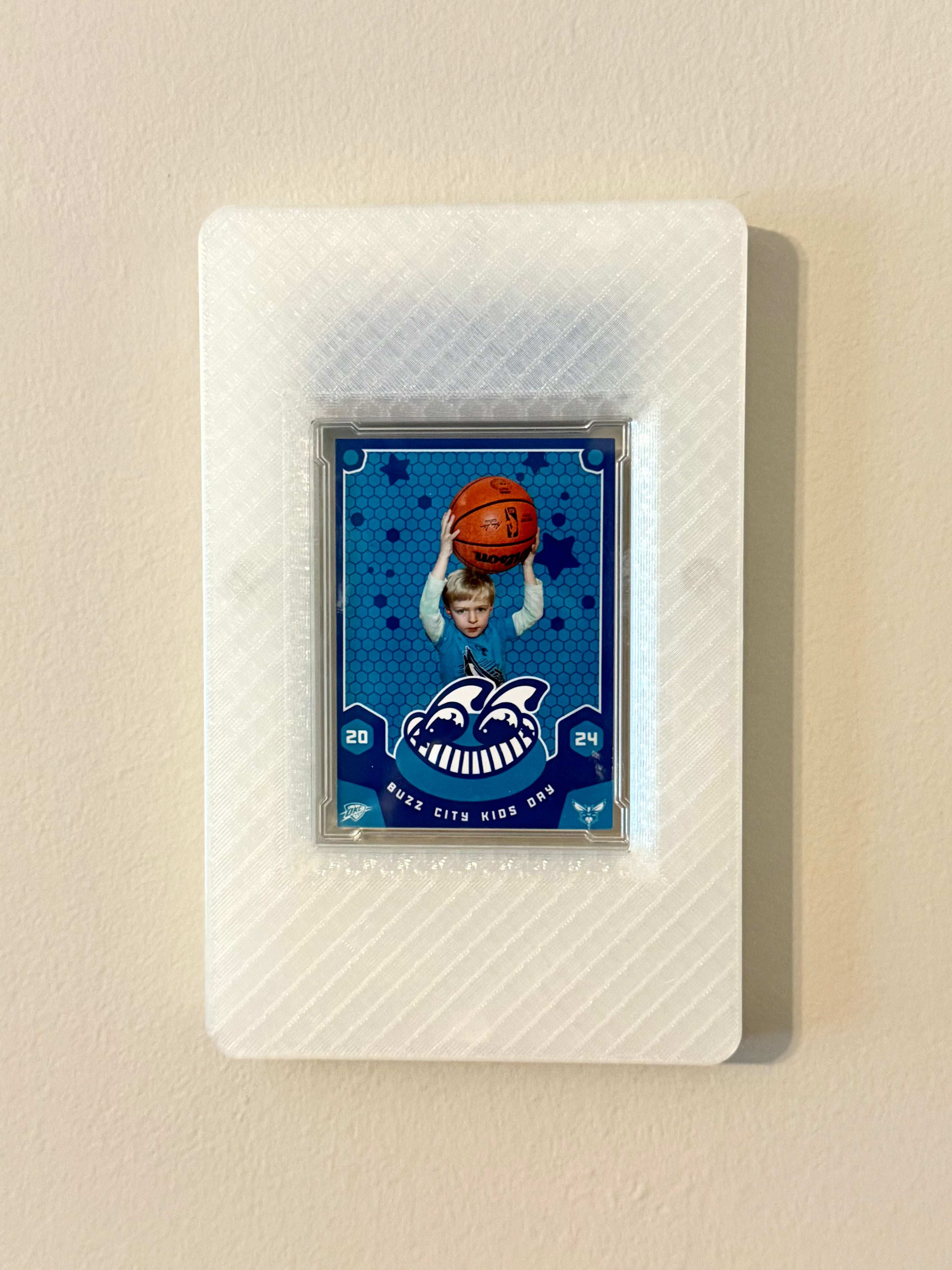 Custom trading card of a child holding a basketball blue background, framed in a translucent SlabGhost frame on a beige wall.
