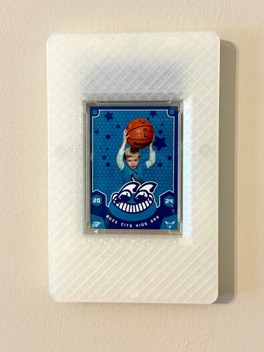 Custom trading card of a child holding a basketball blue background, framed in a translucent SlabGhost frame on a beige wall.